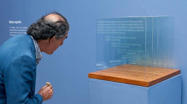 Un hombre con chaqueta azul se inclina hacia una vitrina de cristal con un estante de madera en una exposición de un museo.