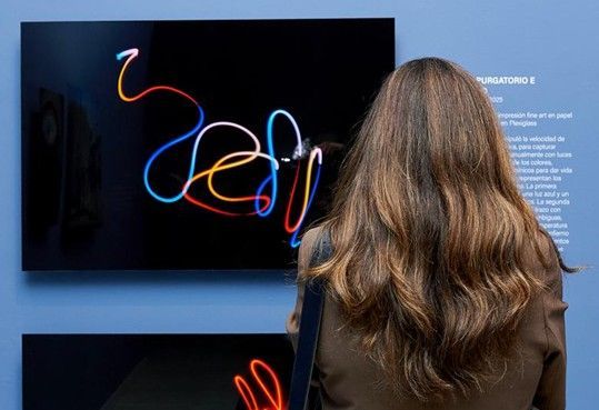 Persona observando una obra de arte abstracta de neón en una pantalla montada en la pared de una galería.