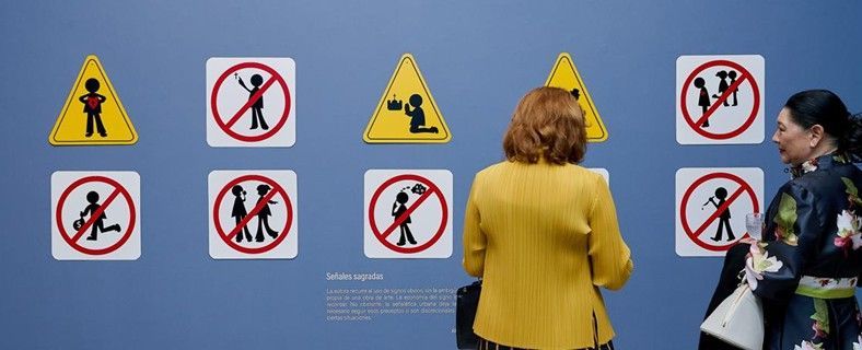 Varias personas observan una pared azul con señales de seguridad amarillas y rojas, dos de ellas en primer plano.