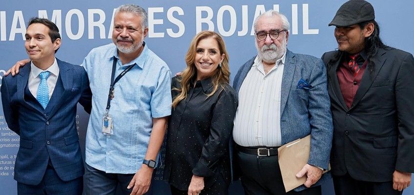 Cinco personas posan en un evento de prensa, de pie frente a un fondo azul con el texto parcial “AMORES BOJ…”.