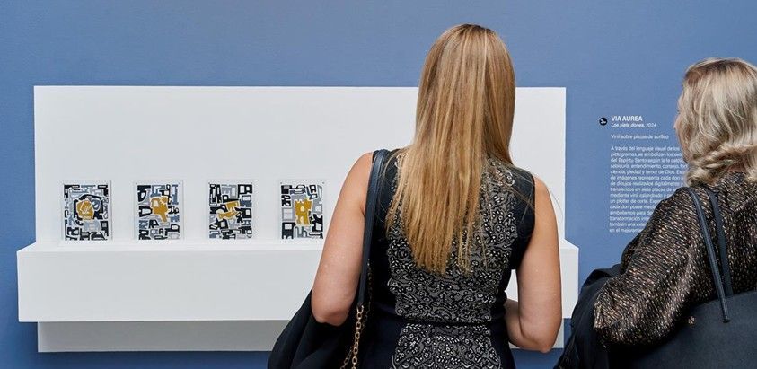 Dos visitantes del museo observan pequeñas obras de arte enmarcadas en una vitrina.