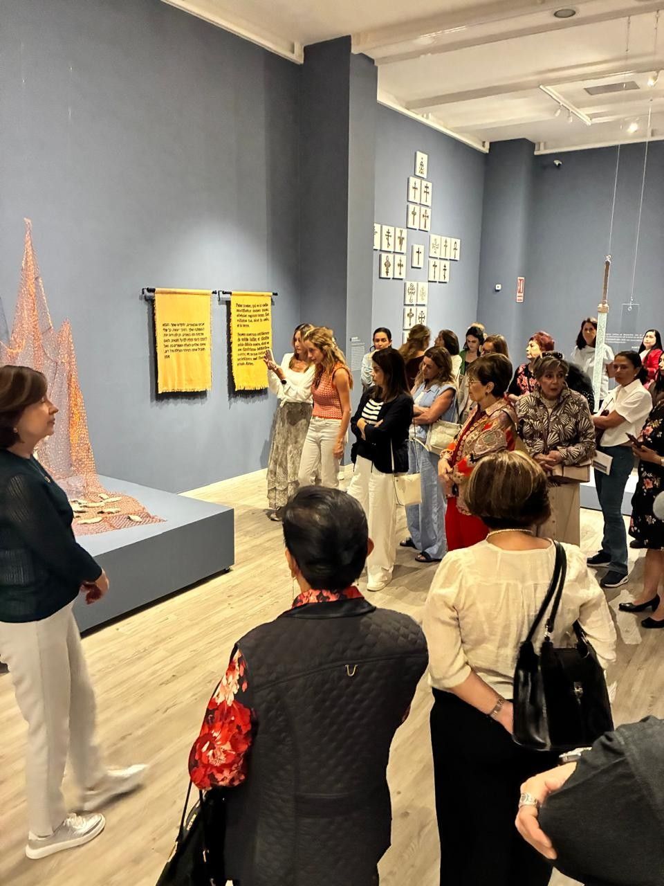 Un grupo de visitantes de un museo escucha a un orador junto a una obra de arte expuesta en una galería.