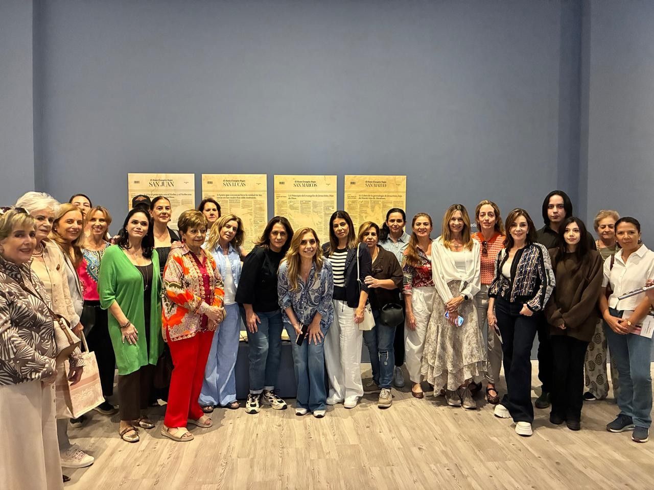 Grupo de personas posando en el interior, frente a paneles informativos; algunas visten atuendos coloridos.