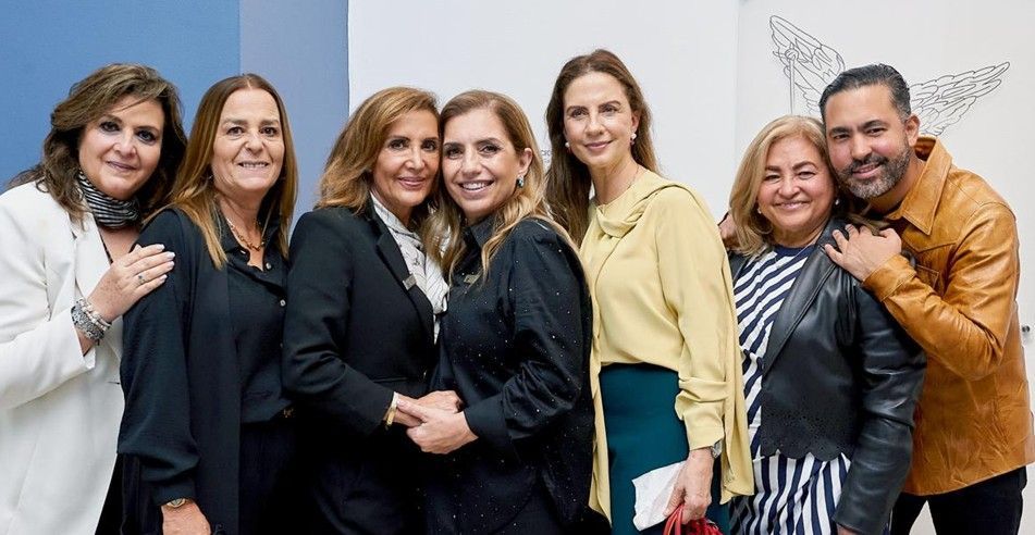 Grupo de siete personas sonriendo y posando juntas frente a un fondo azul claro y blanco.