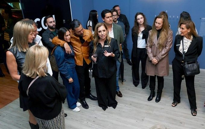Un grupo de personas se reunió en el interior, escuchando a una mujer rubia que hablaba al frente.