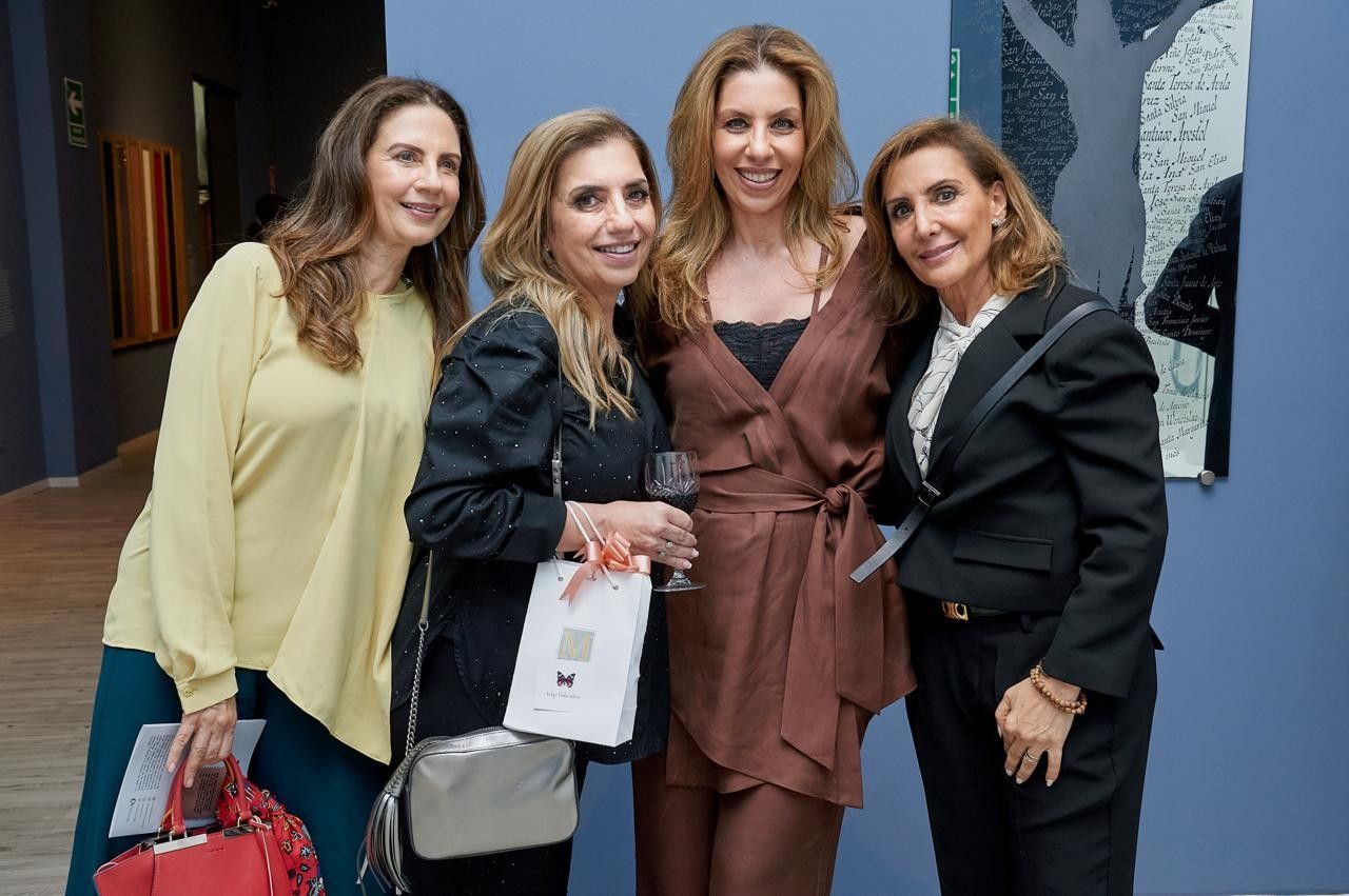 Cuatro personas sonriendo y posando en el interior de un evento, sosteniendo papeles y una bolsa de tela.