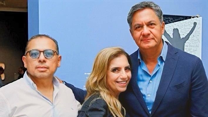 Tres personas sonrientes posando en el interior, con una pared azul y una obra de arte abstracto detrás.
