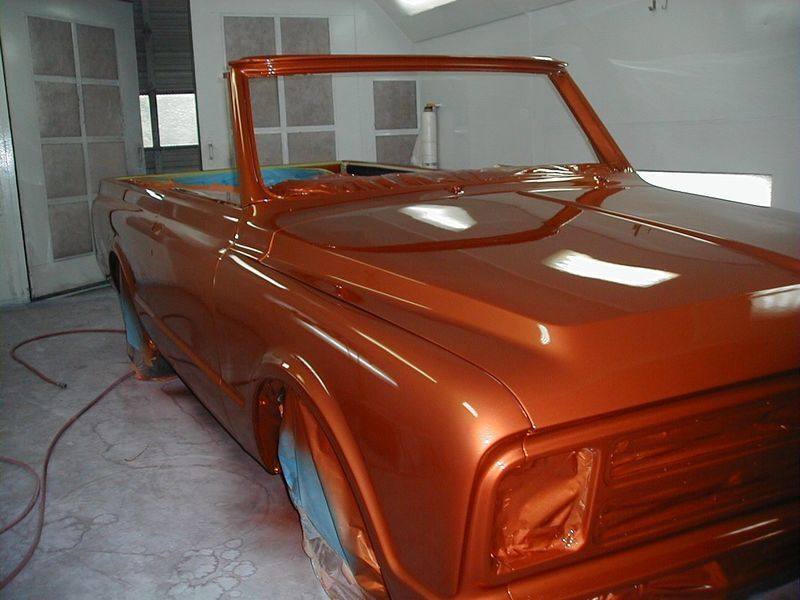 An orange car is being painted in a garage