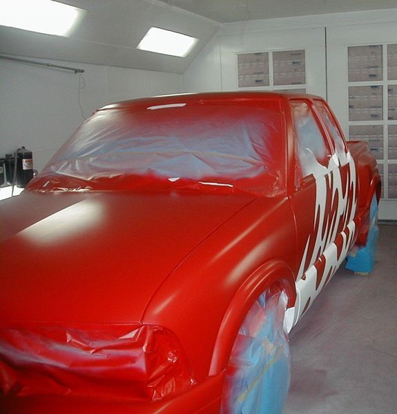 A red car is being painted in a garage
