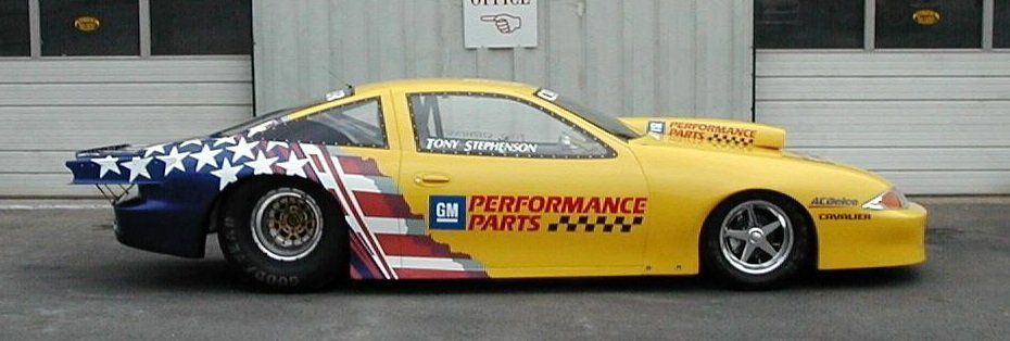 A yellow gm performance parts car is parked in front of a garage