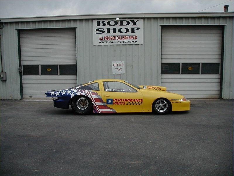 A yellow race car is parked in front of a body shop