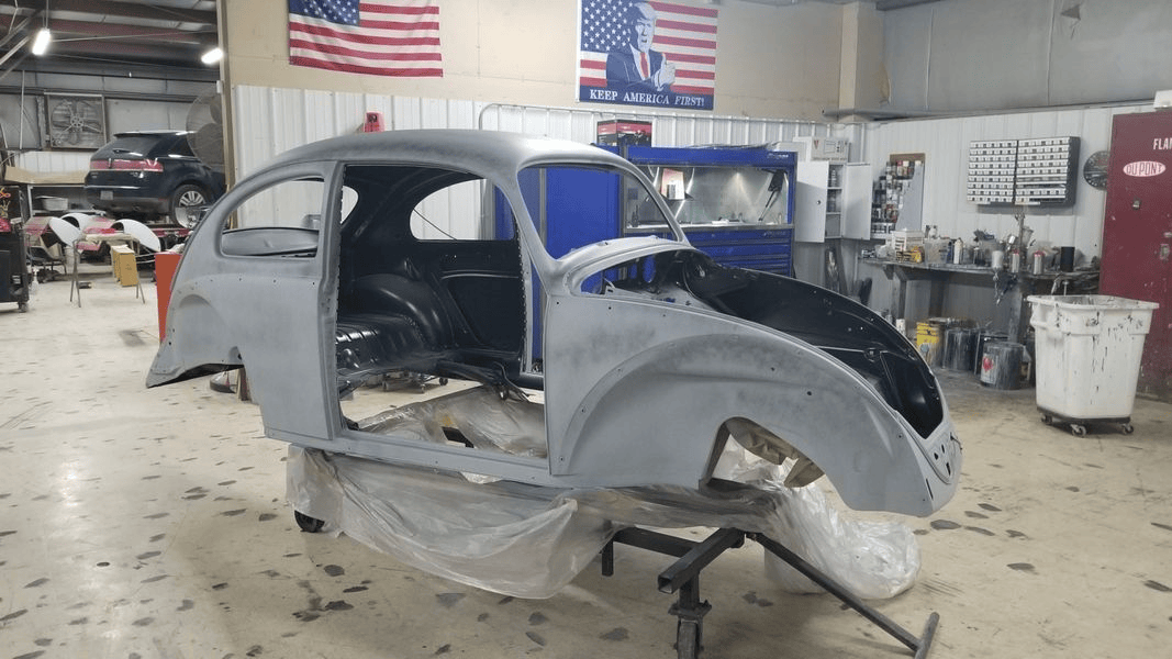 A volkswagen beetle is being restored in a garage.