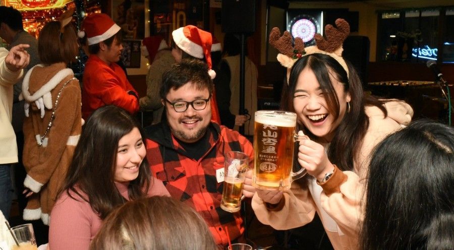 Um grupo de pessoas está sentado à mesa segurando copos de cerveja.
