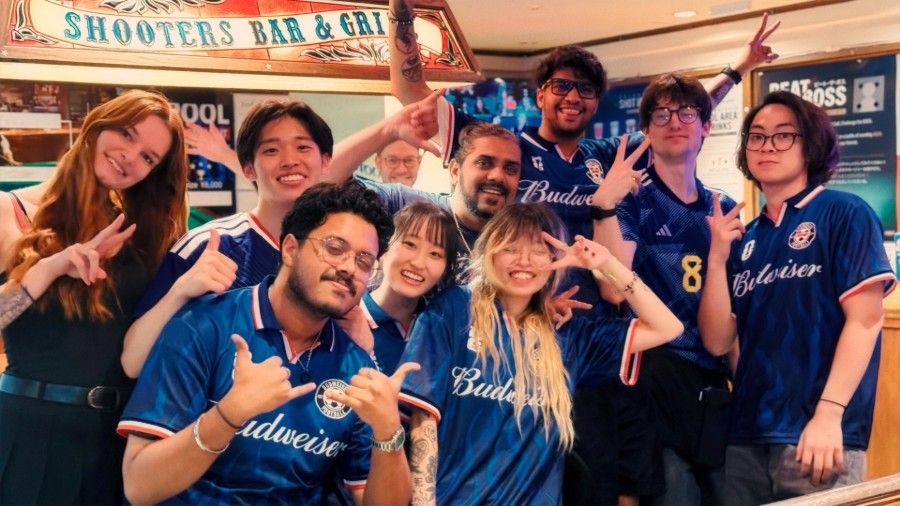 Group of friends in blue Budweiser shirts posing and smiling in front of a bar sign.