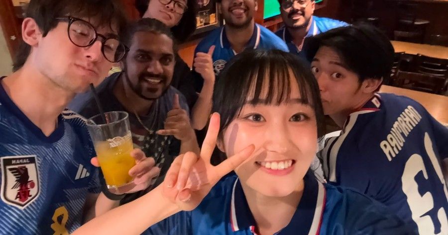 Group of friends in Japan national soccer team jerseys taking a selfie at a sports bar, smiling and 