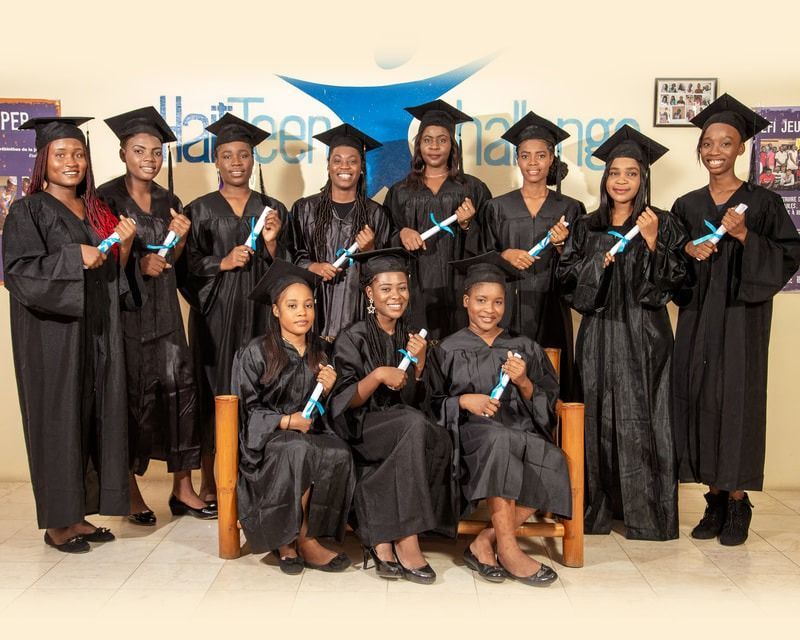 Eleven graduates in black caps and gowns pose for a photo at Haiti Teen Challenge, holding diplomas.