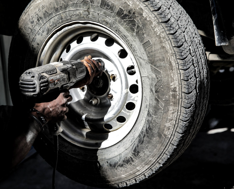 A person uses a power tool to tighten the lug nuts on a vehicle's tire in a garage.