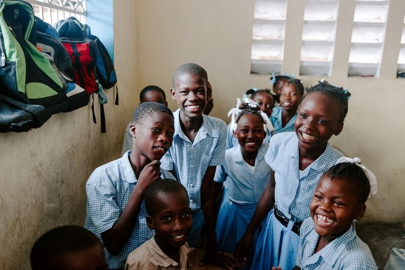 A group of students in blue uniforms smiling in a brightly lit classroom.