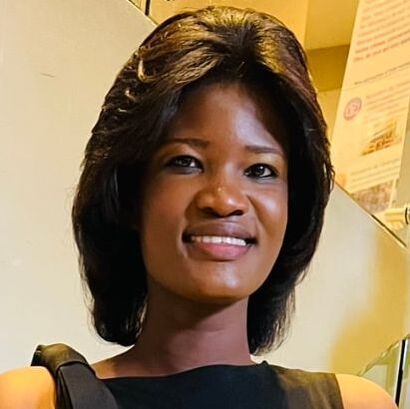 Portrait of a smiling person with dark, shoulder-length hair wearing a black sleeveless top, in an indoor setting.