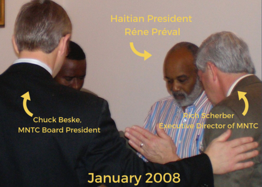 Men pray over Haitian President René Préval in January 2008, including MNTC leaders Chuck Beske and Rich Scherber.