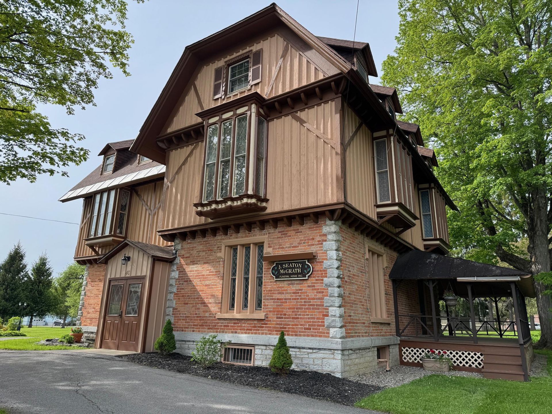 Historic brick-and-wood house with steep roof and green shutters, surrounded by trees
