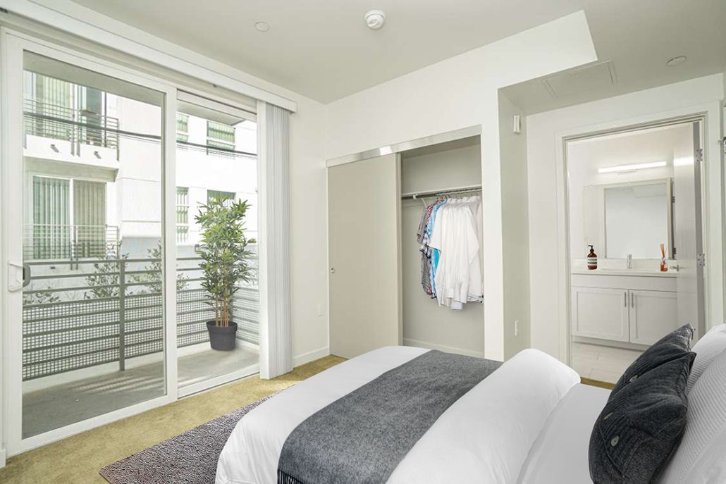 A bedroom with a large bed , sliding glass doors , a balcony and a closet.
