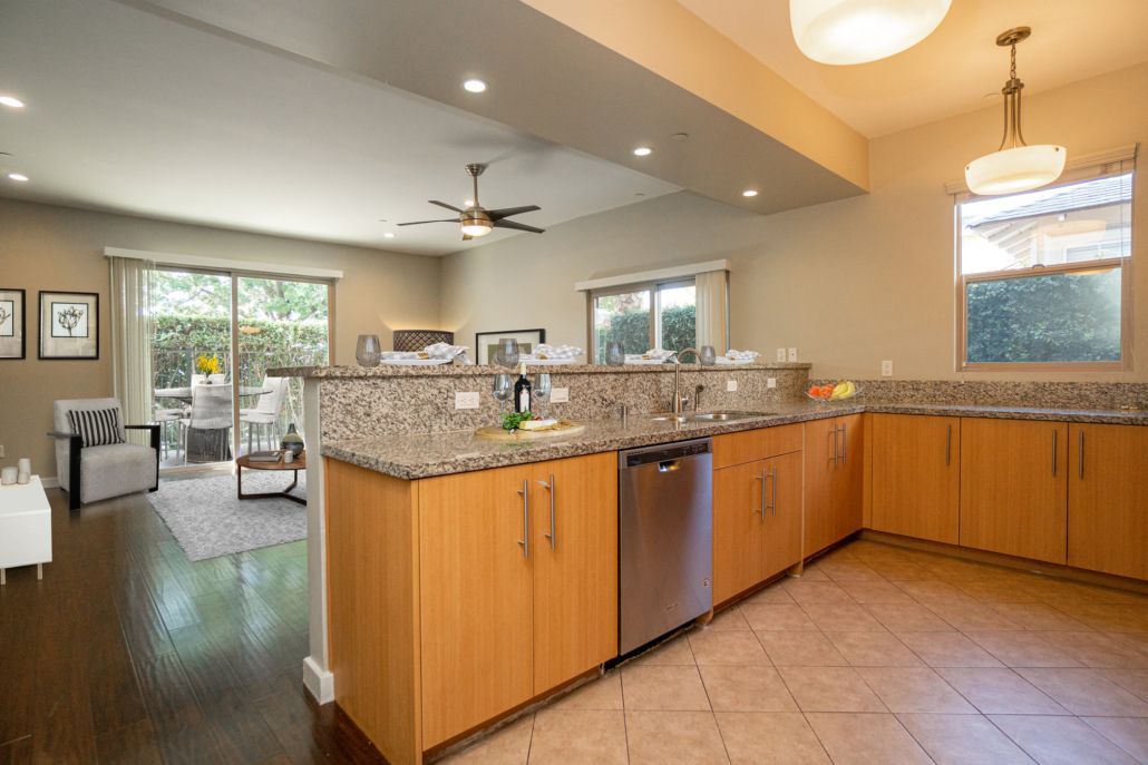 A kitchen with wooden cabinets , granite counter tops , stainless steel appliances and a ceiling fan.