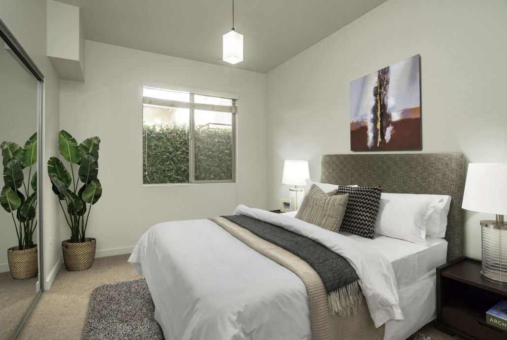 A bedroom with a large bed , a plant , a mirror and a painting on the wall.