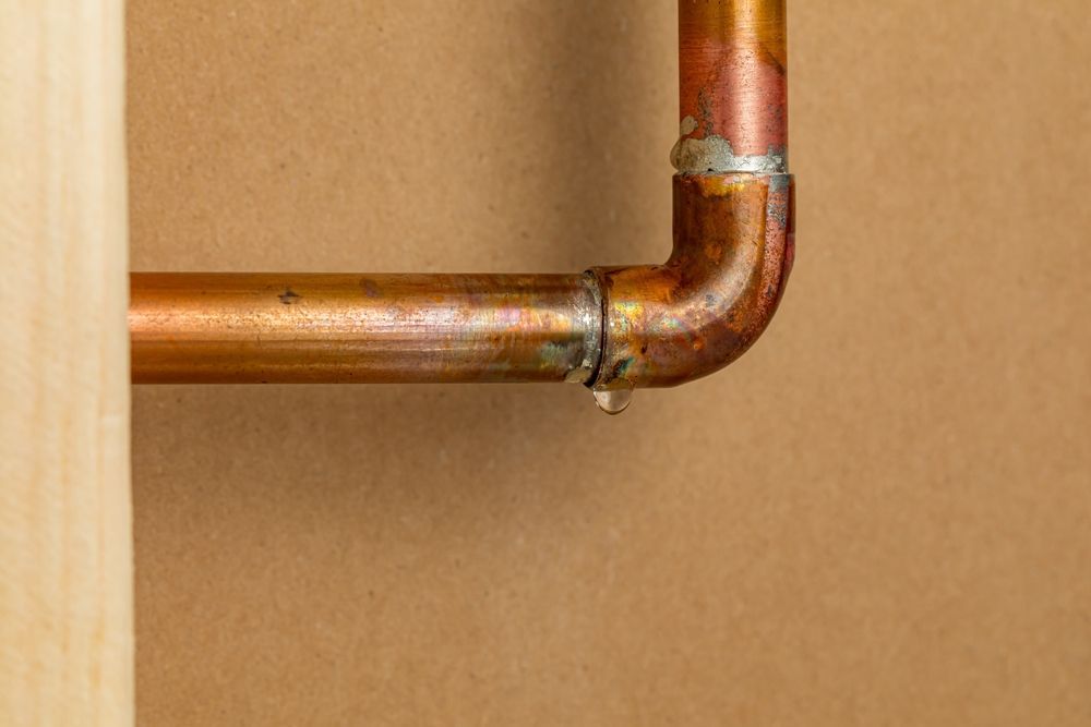 A close up of a copper pipe with a drop of water coming out of it.