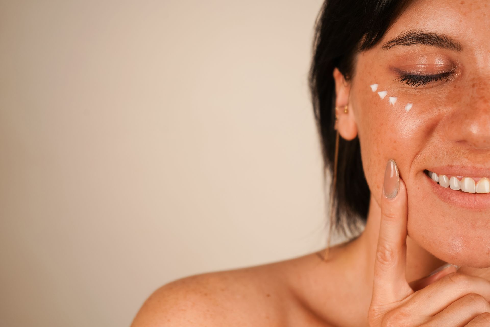 A girl with clean skin applies cream to her cheeks.