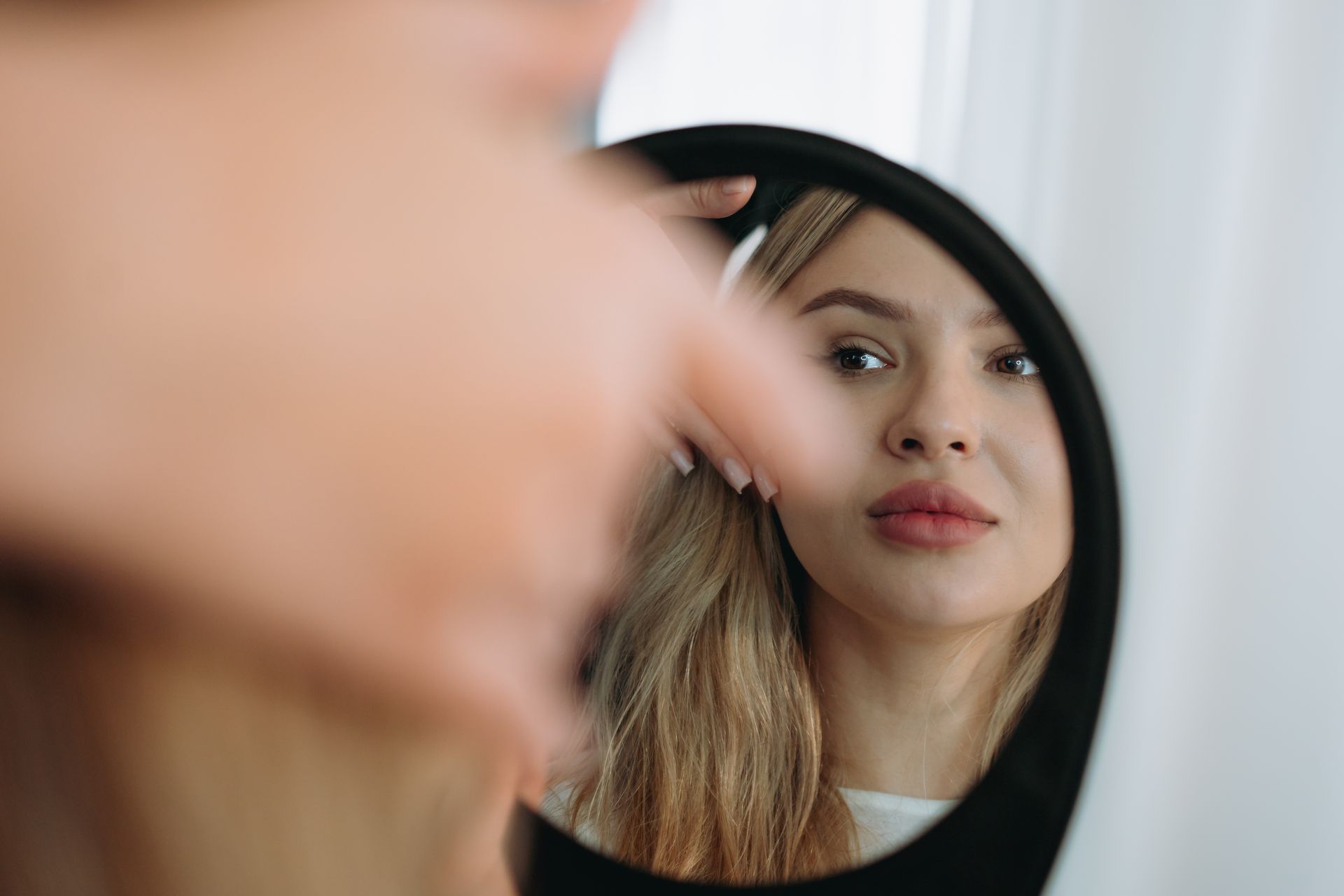 young woman looking in a mirror after facial rejuvenation procedure. young woman looking in a mirror after facial rejuvenation procedure.