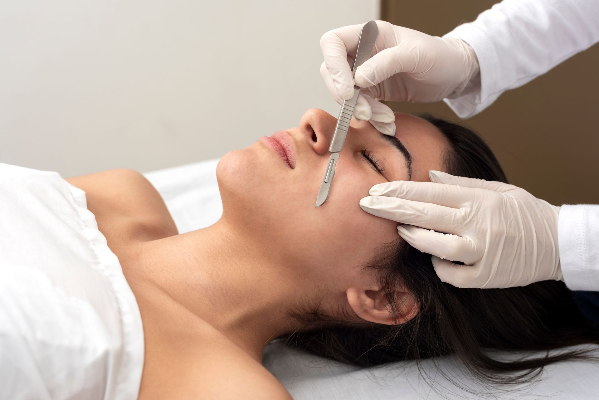 young woman on a table in a beauty center performing a beauty treatment for facial skin with the dermaplaning technique young woman on a table in a beauty center performing a beauty treatment for facial skin with the dermaplaning technique