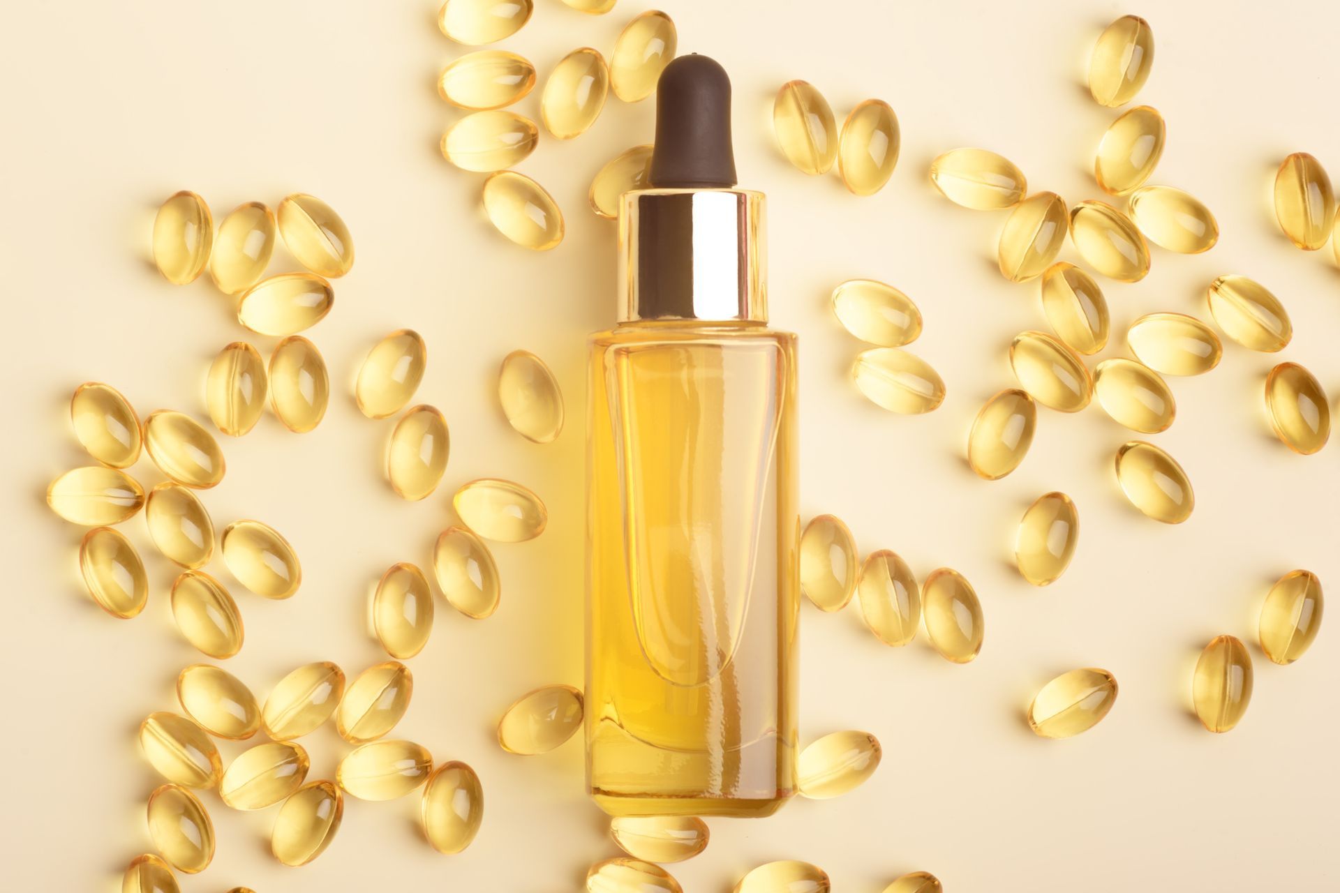 Yellow oil bottle with dropper surrounded by scattered capsules.