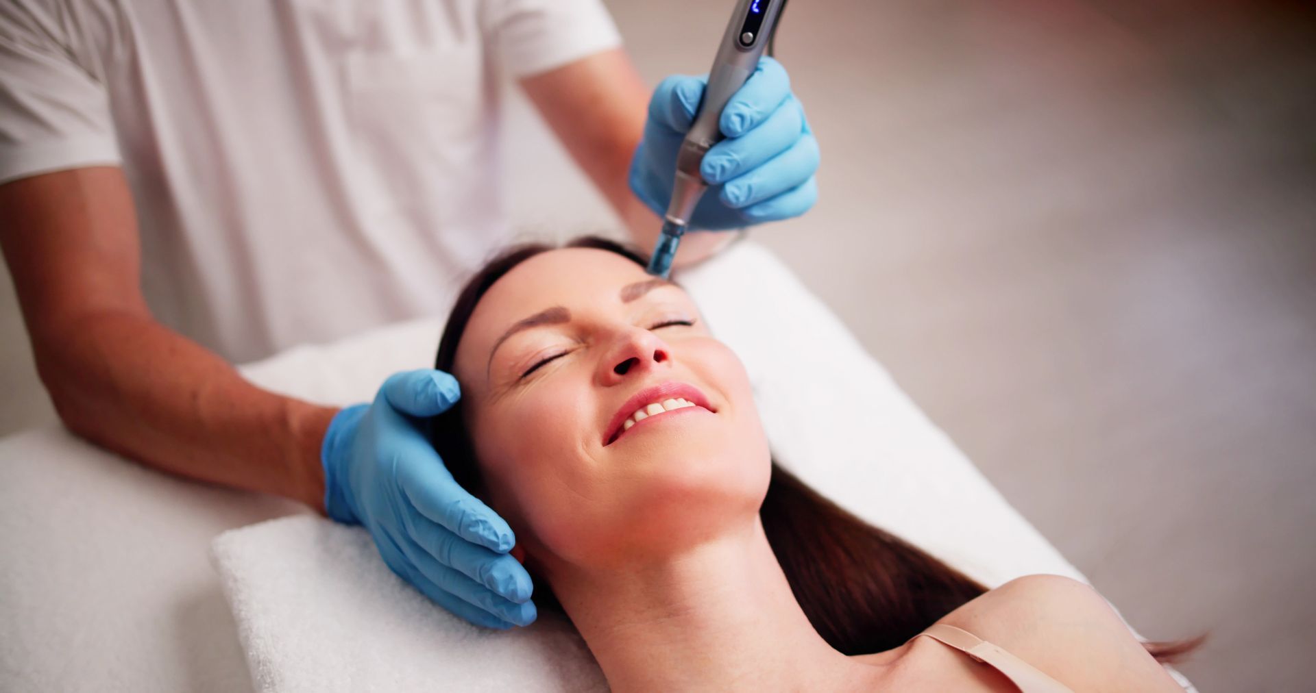 Person receiving facial treatment with a handheld device, blue gloves, white shirt.