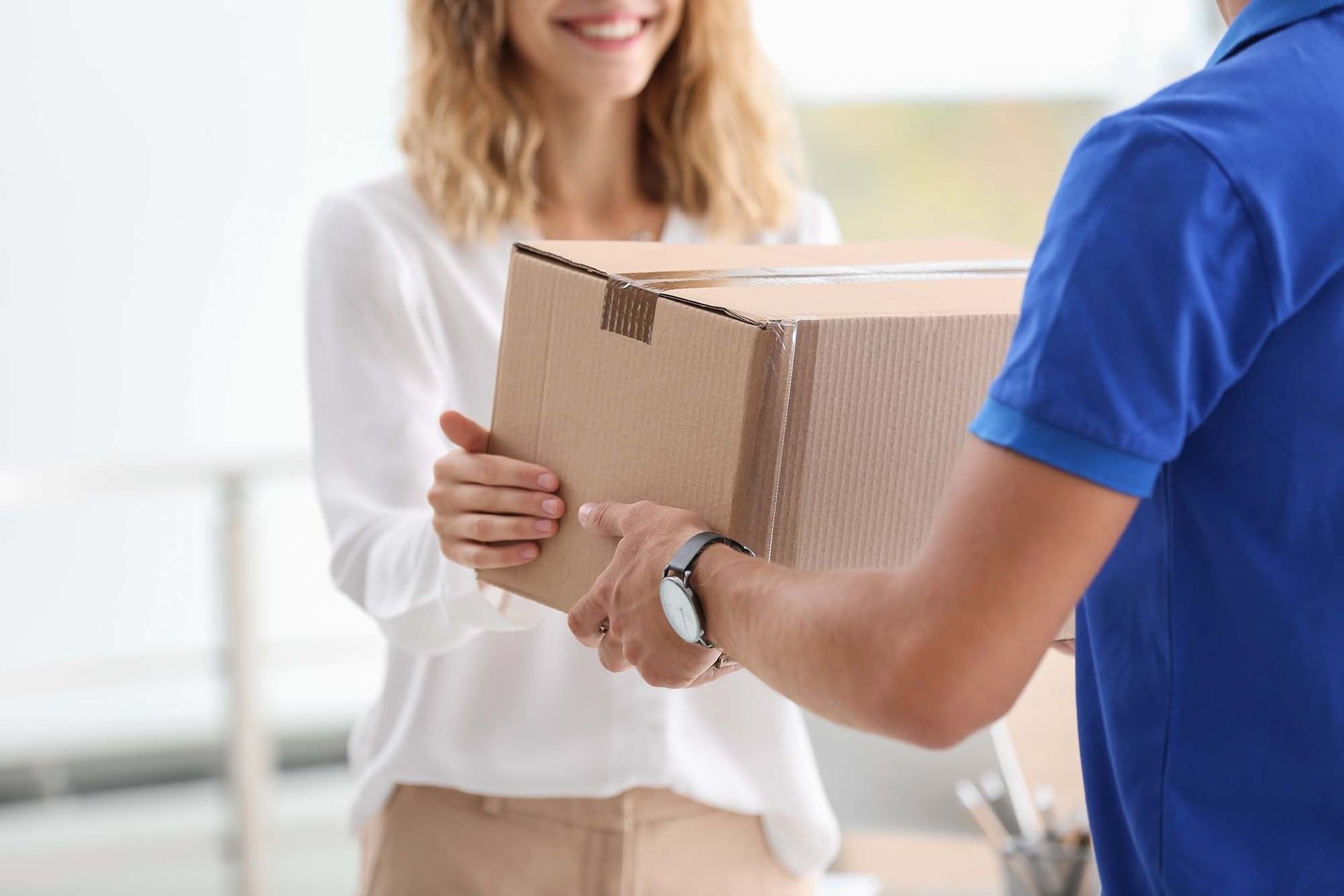 Person handing a cardboard package to a smiling customer indoors