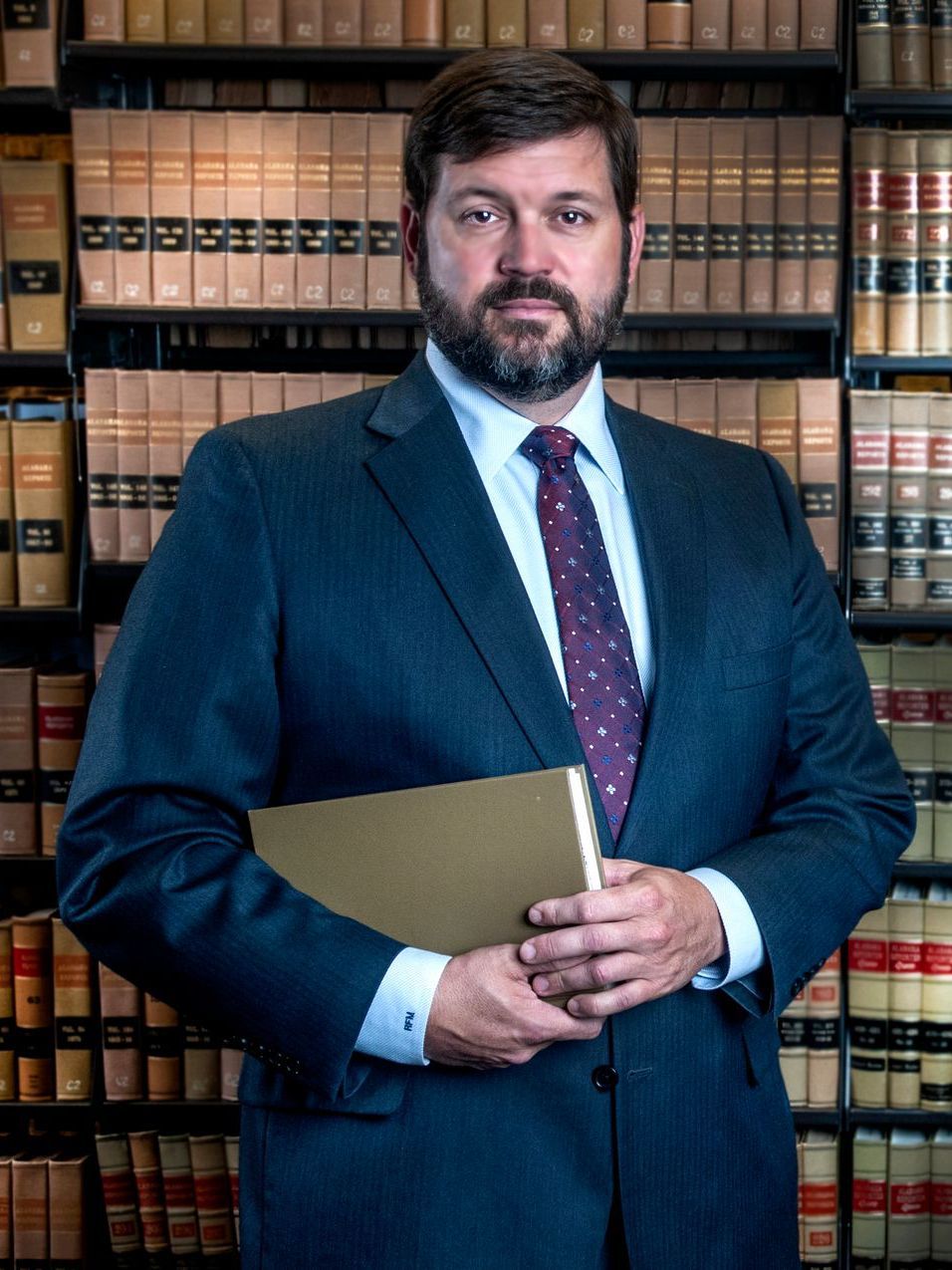 Man in suit holding open book, smiling in a library.