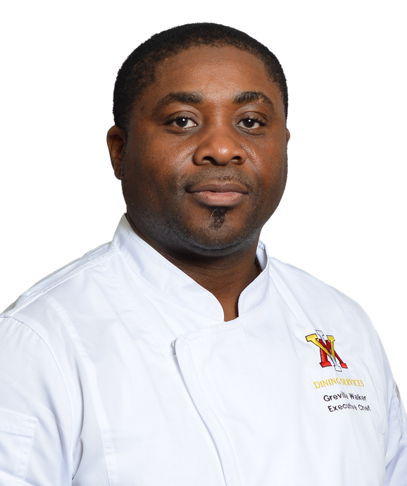 A person in a white chef’s uniform stands facing forward.