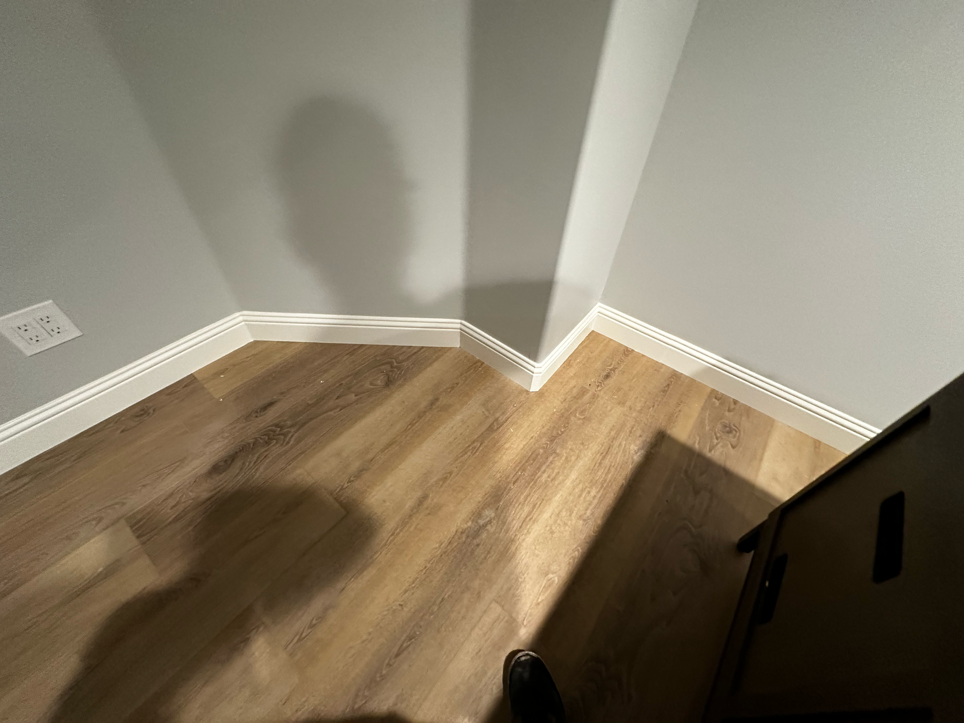 A corner of a room with hardwood floors and white trim.
