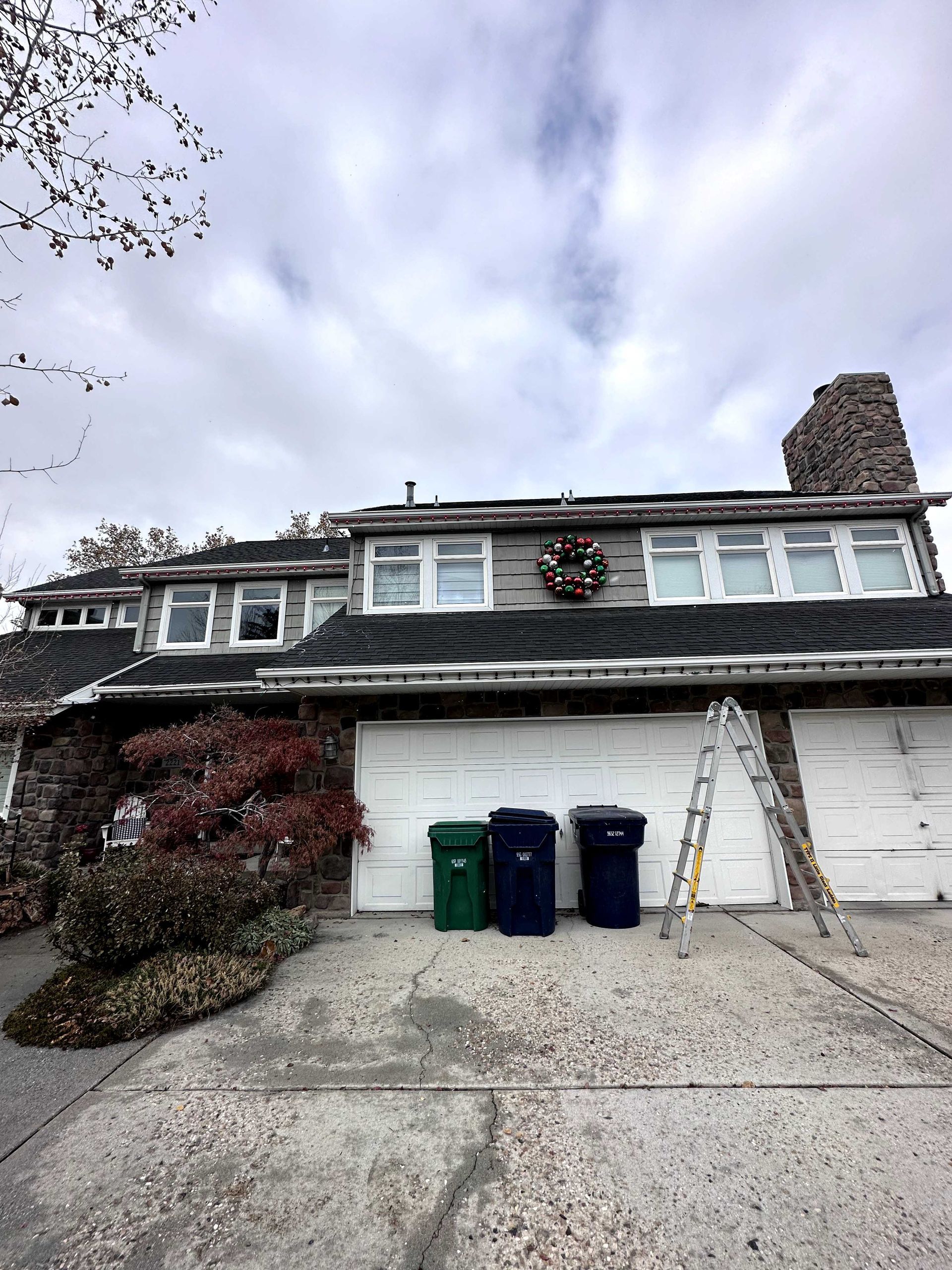 A house with a wreath on the roof and trash cans in front of it.