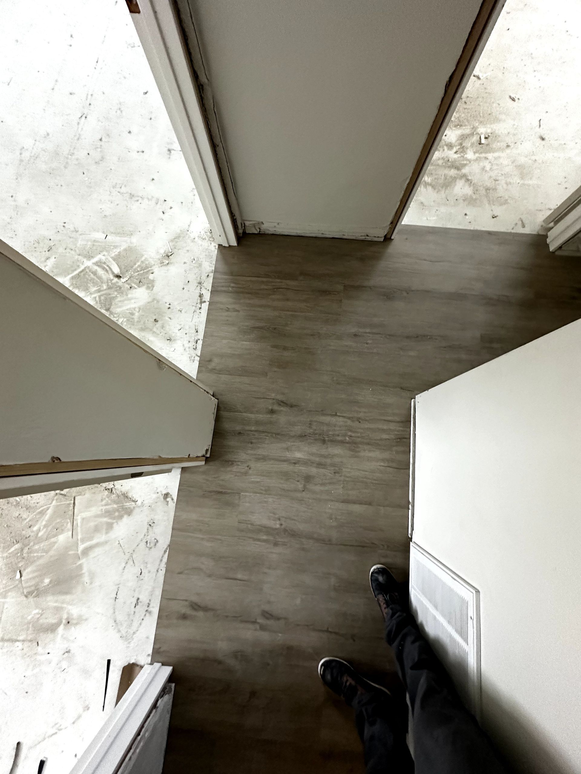 A person is standing on a wooden floor in a hallway.