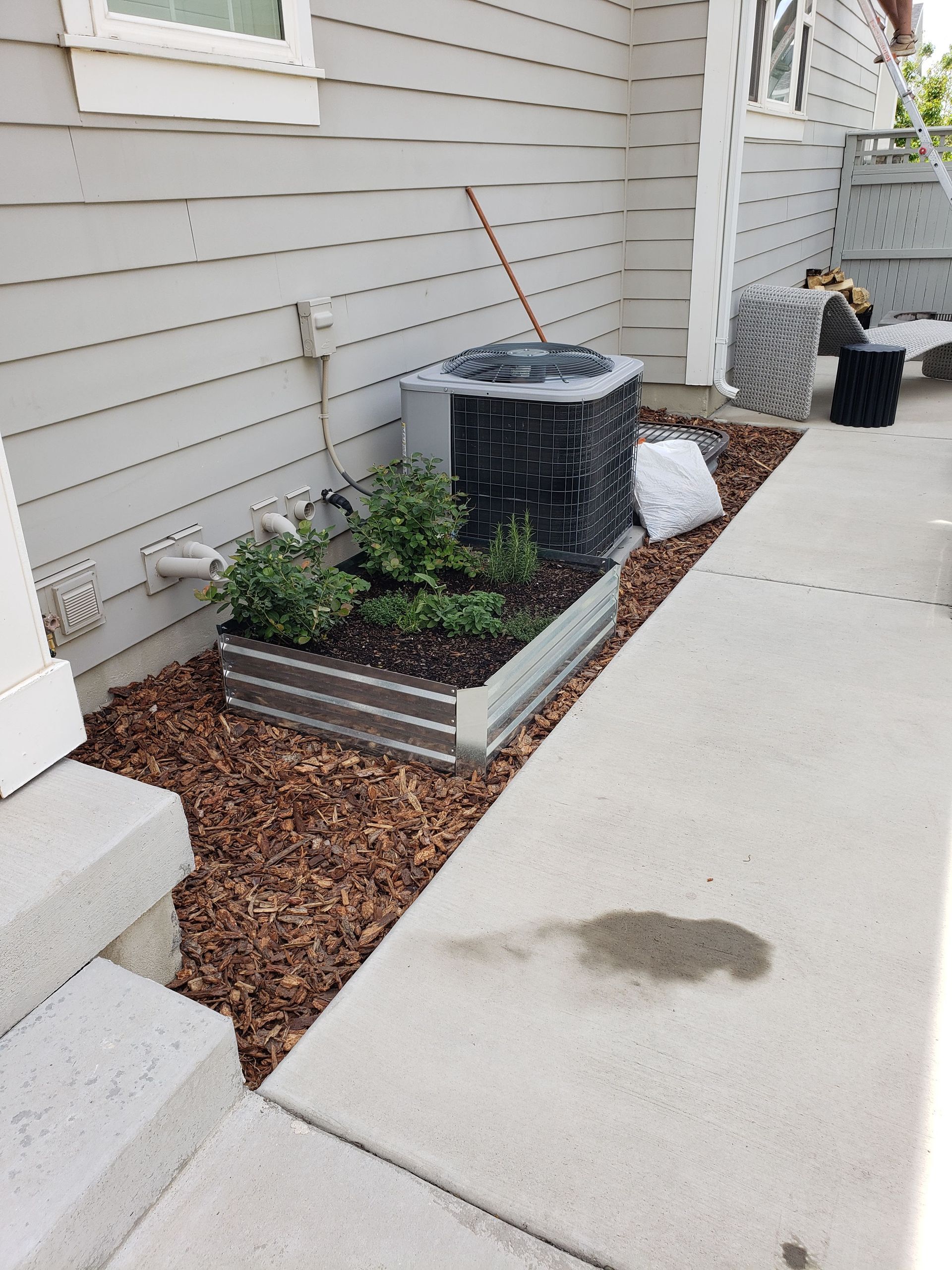 An air conditioner is sitting in a planter on the side of a house.
