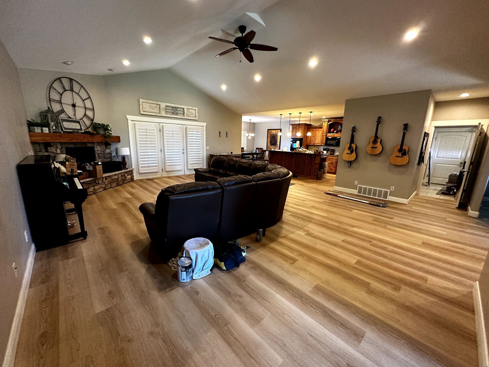 A living room with a couch , piano , guitars and a ceiling fan.