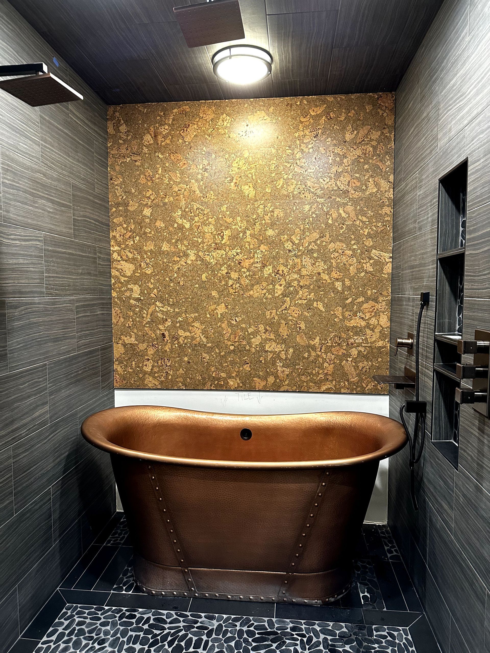 A bathroom with a copper bathtub and a cork wall