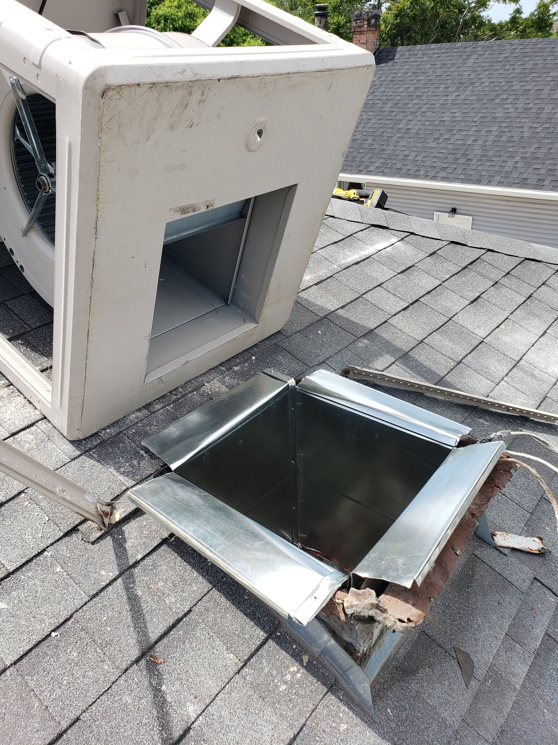 A fan is sitting on top of a roof next to a hole in the roof.