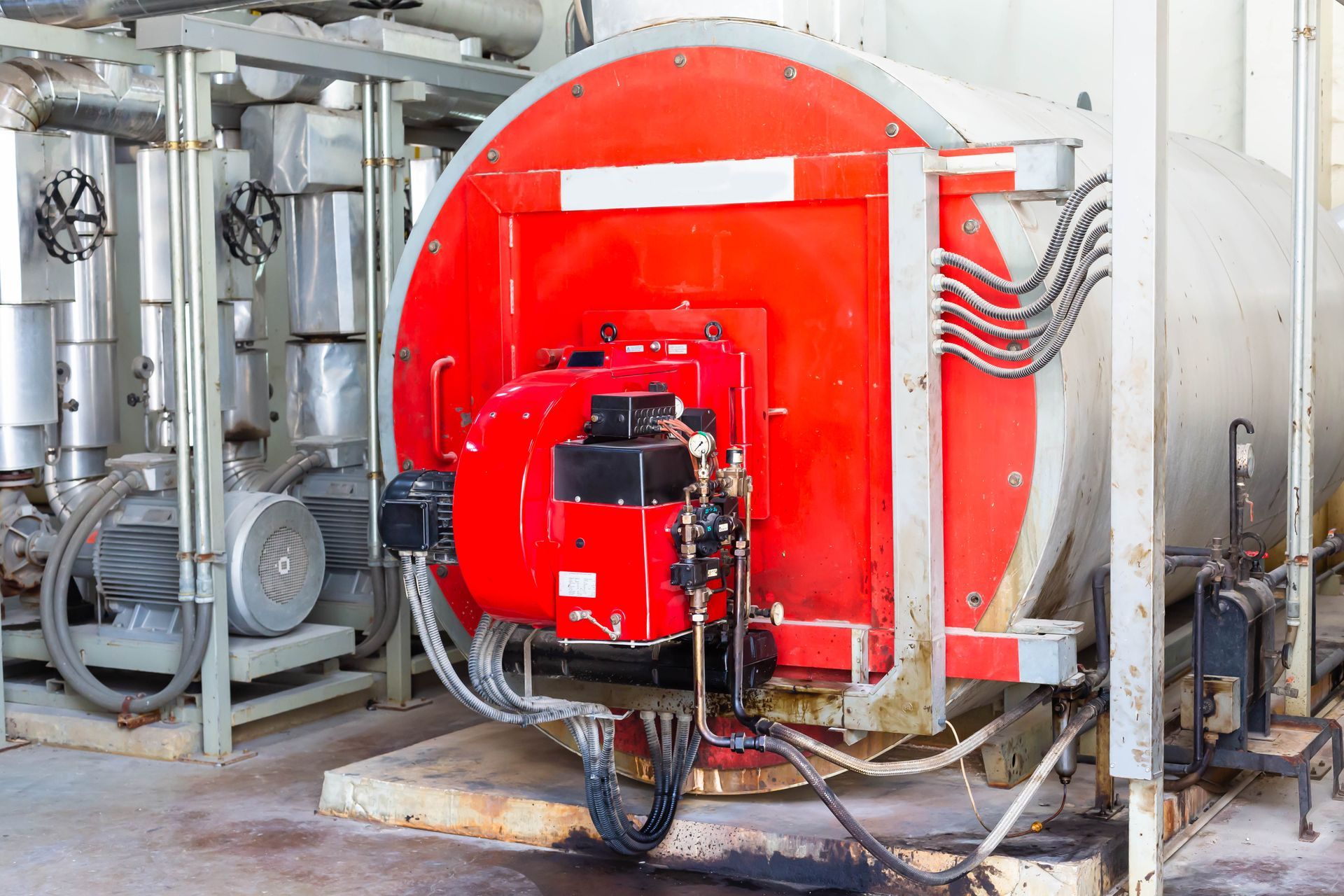 Industrial red firetube boiler with gauges, wiring, and pressure valves in a mechanical boiler room