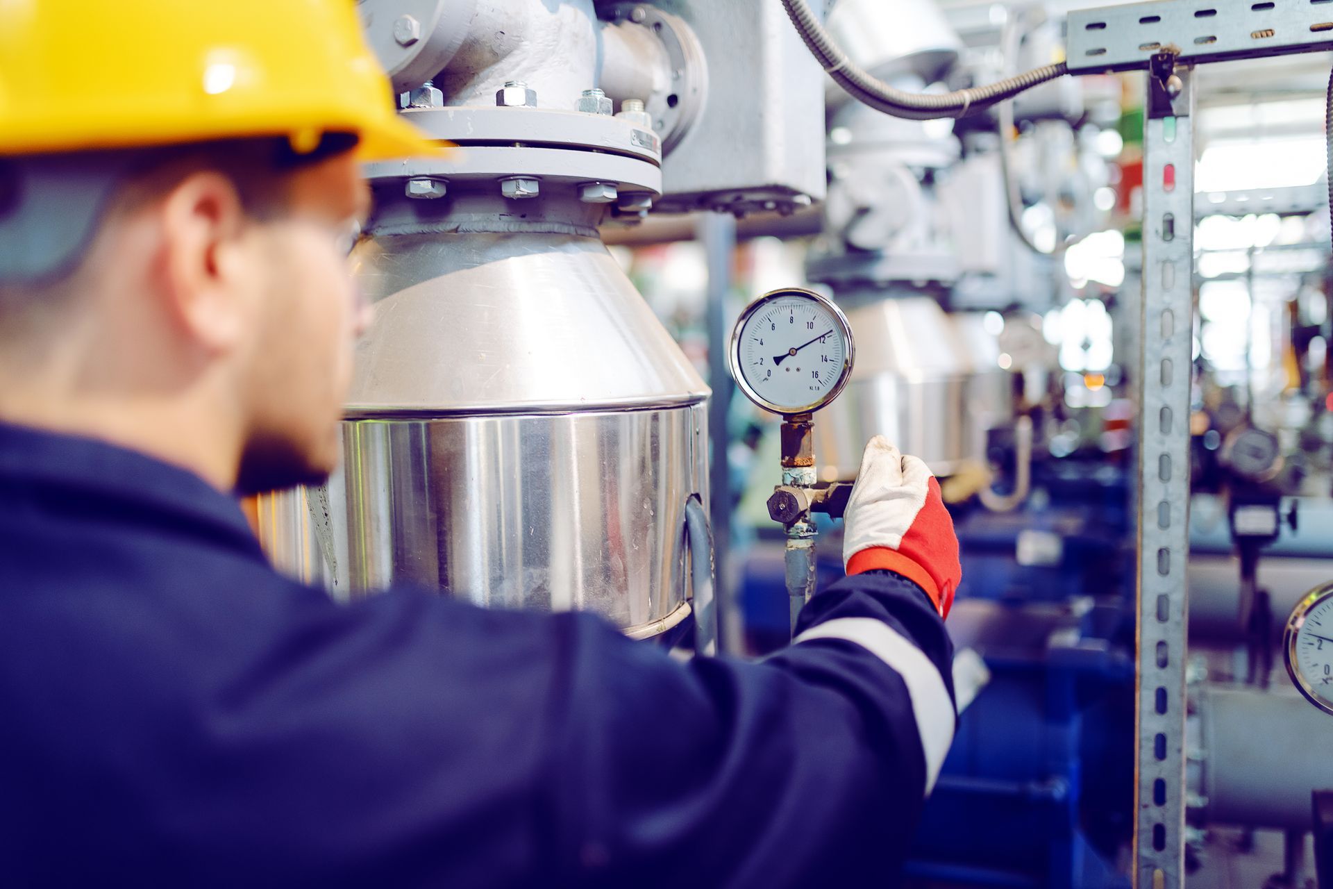 Industrial worker adjusting pressure gauge on metal tank in a mechanical room.