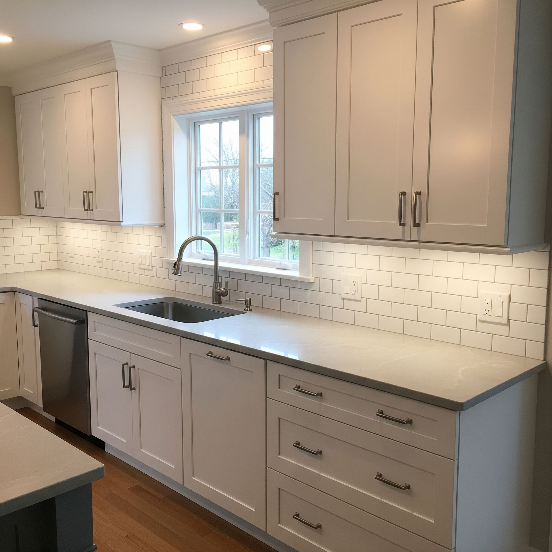Bright kitchen with white cabinets, countertops, and tile backsplash. Stainless steel sink and appliances.