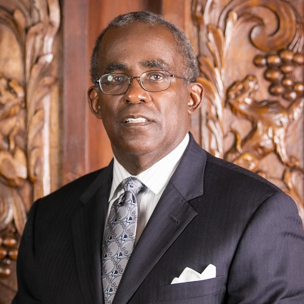 A man in a suit and tie is standing in front of a carved wooden wall.
