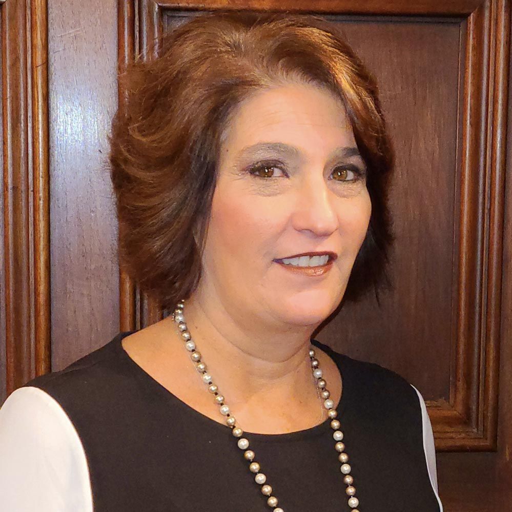 A woman wearing a black shirt and a pearl necklace is smiling for the camera.