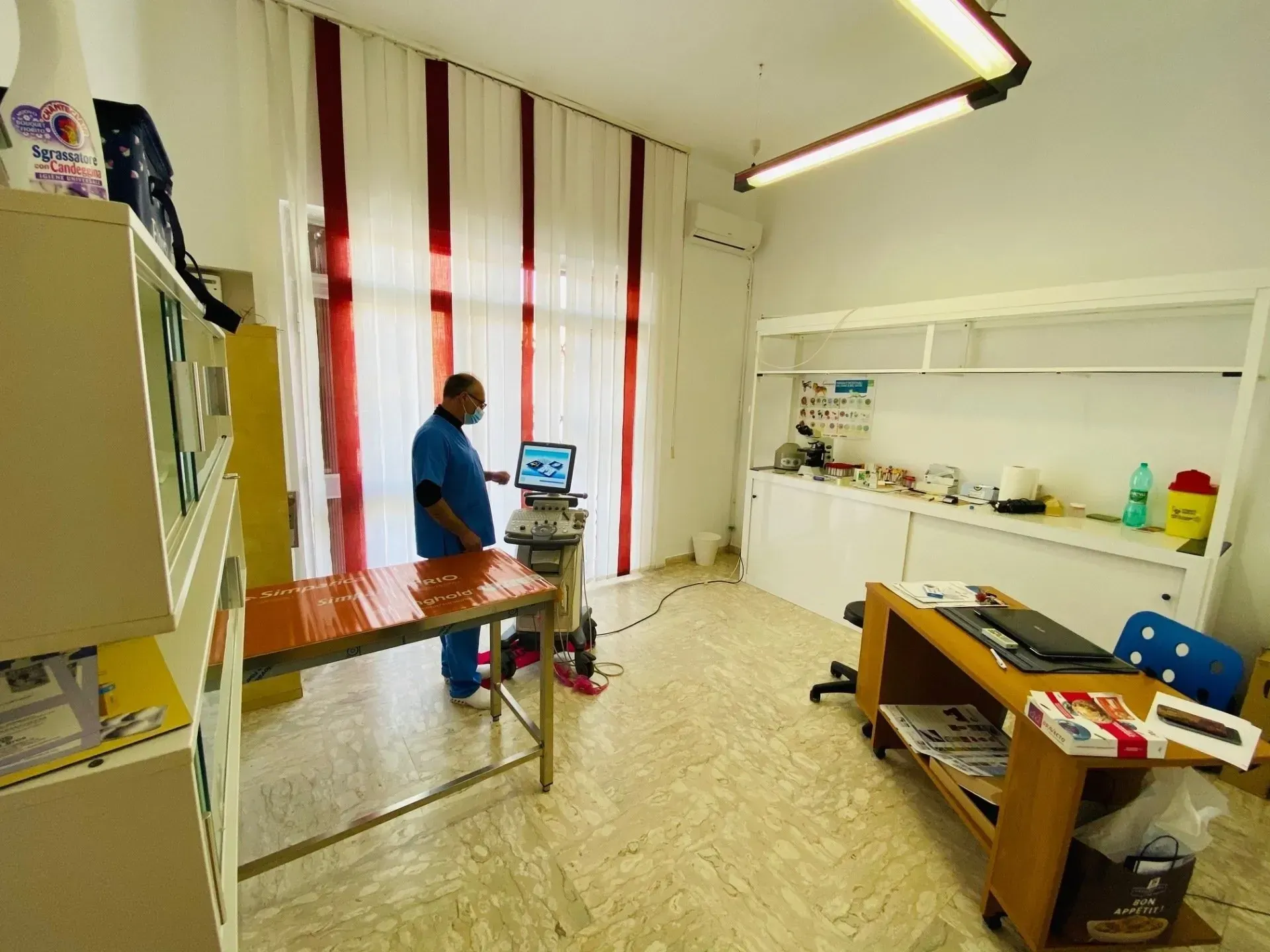 Un professionista in camice chirurgico utilizza un apparecchio a ultrasuoni all'interno di una sala per visite mediche.